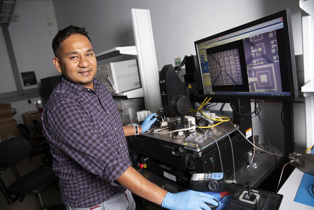 Georgia Tech ECE Professor Asif Khan in his lab. Looking at the camera with microelectronics under a microscope on a computer screen.
