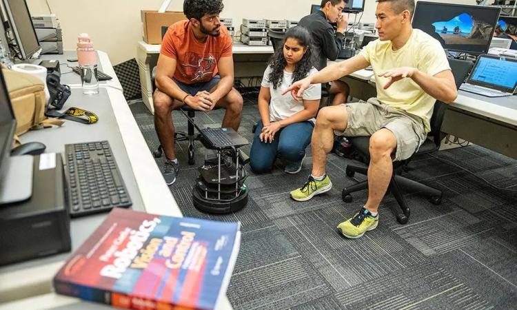 ECE students in a class room discussing a robot