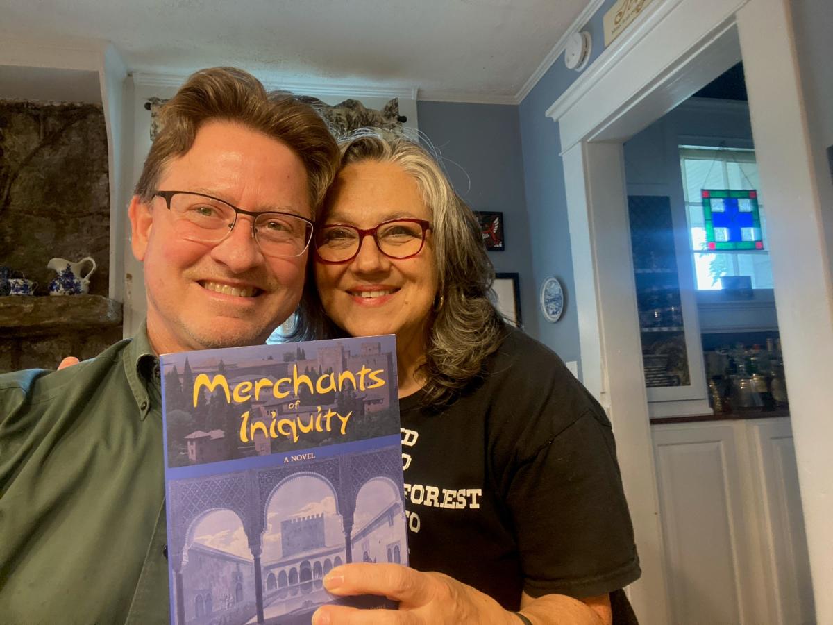 John Cressler and his wife posing with his book Merchant of Iniquity 