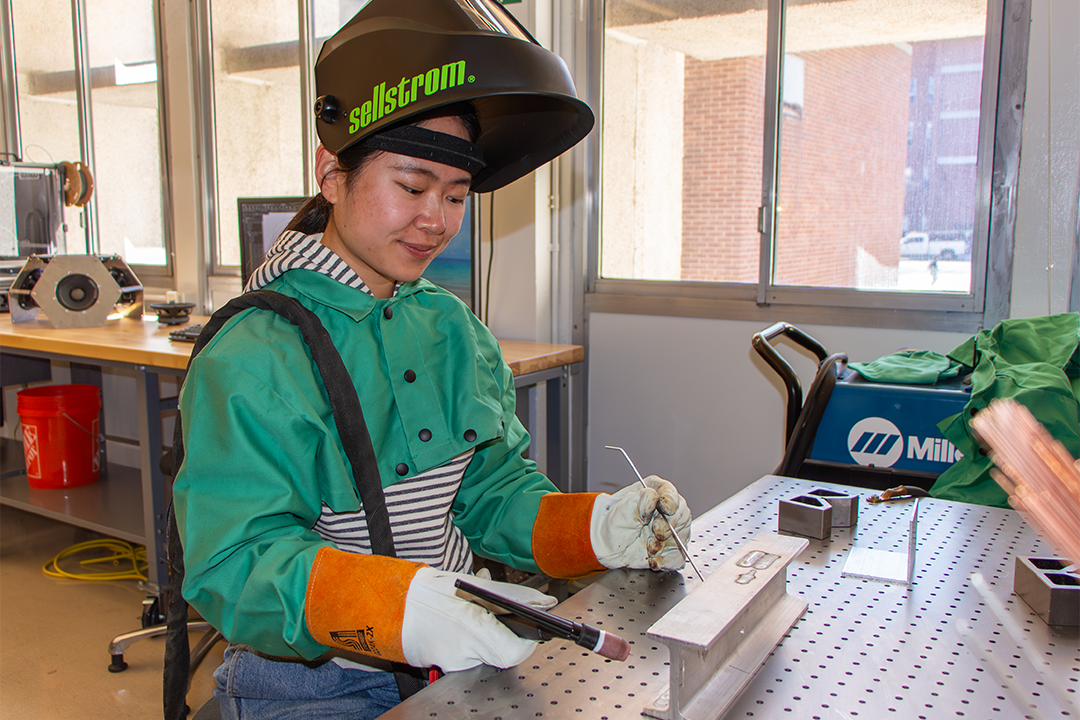 Hannah Xiao practices welding techniques in the ECE mechanical shop as she builds safe, high‑voltage enclosure components for her research.